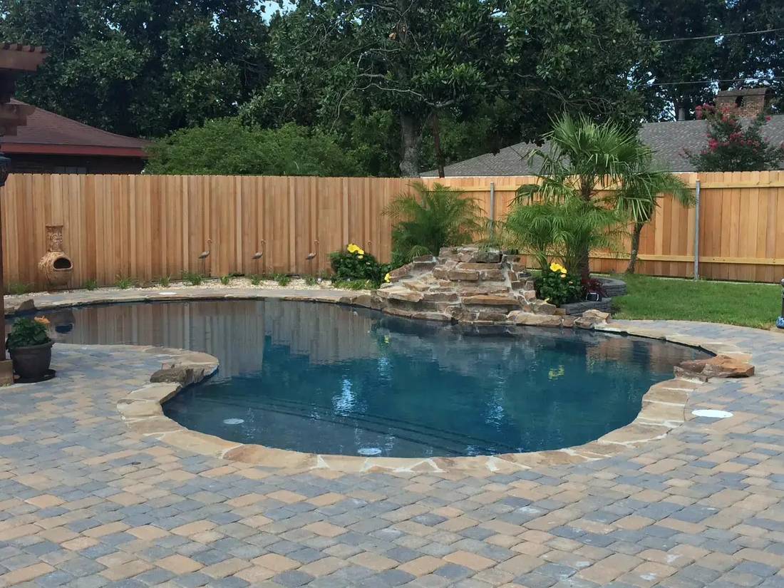 Free-form pool with a flagstone waterfall and paver deck