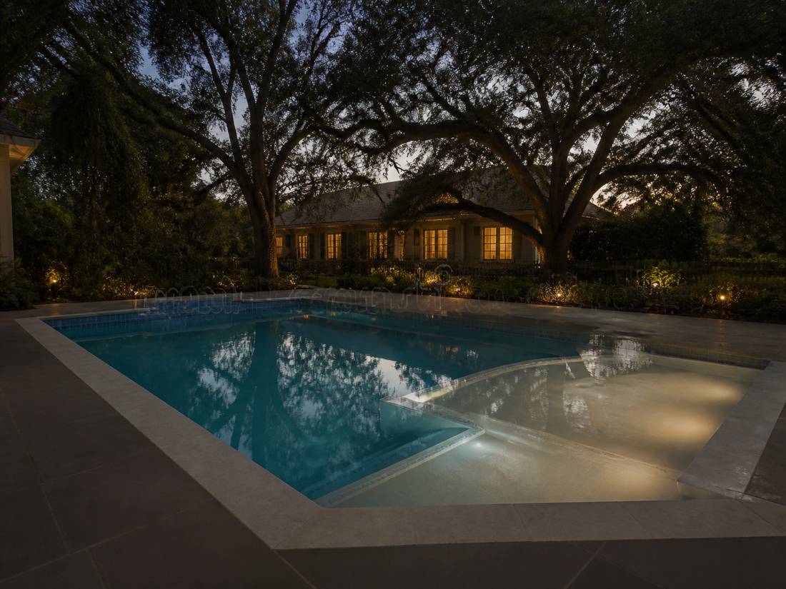 Evening Louisiana pool with a shallow spa shelf and warm deck lighting